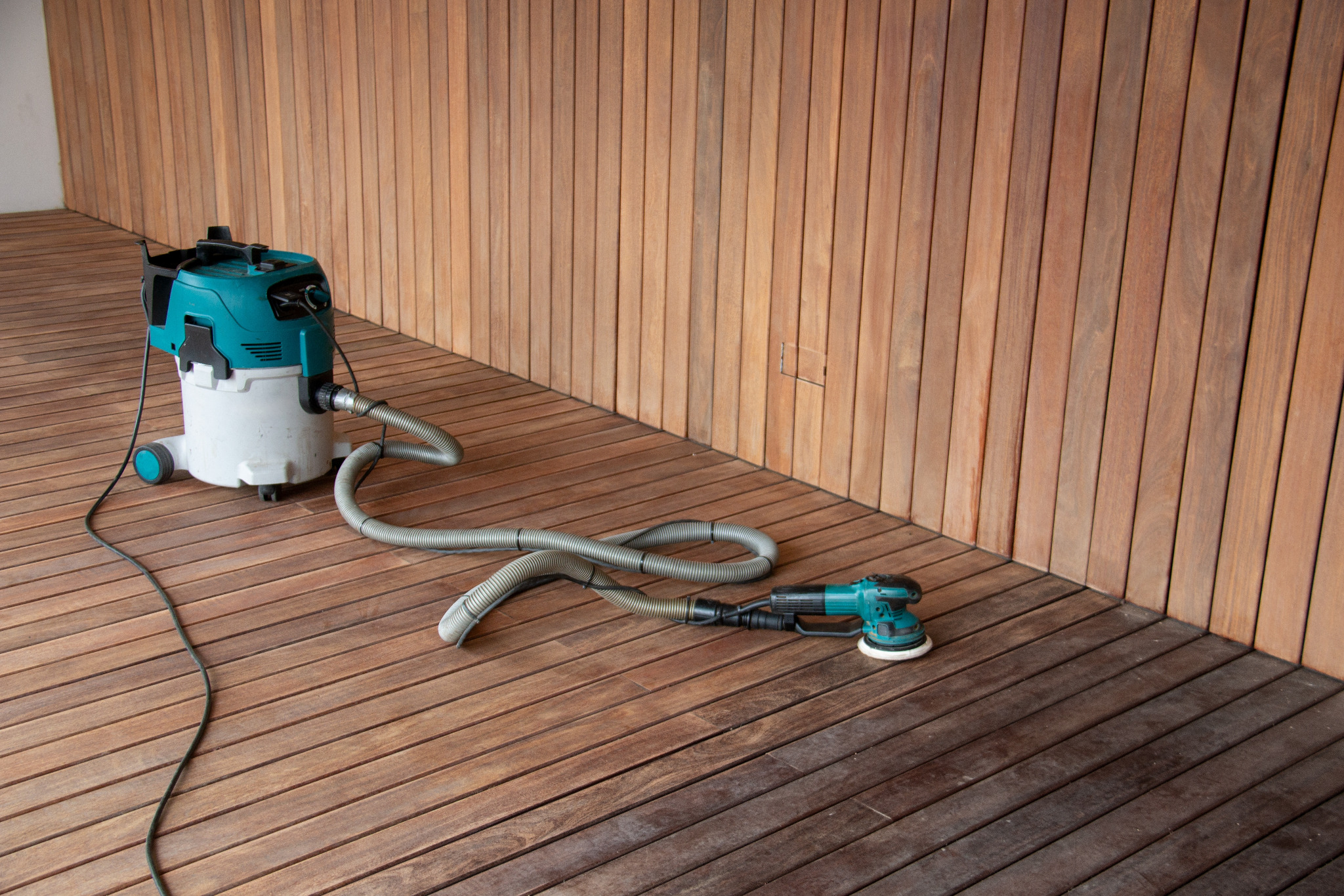 Dust-controlled Deck Sanding in Chelsea on an exterior hardwood timber decking floor, with a vacuum extractor and orbital sander ready for use.