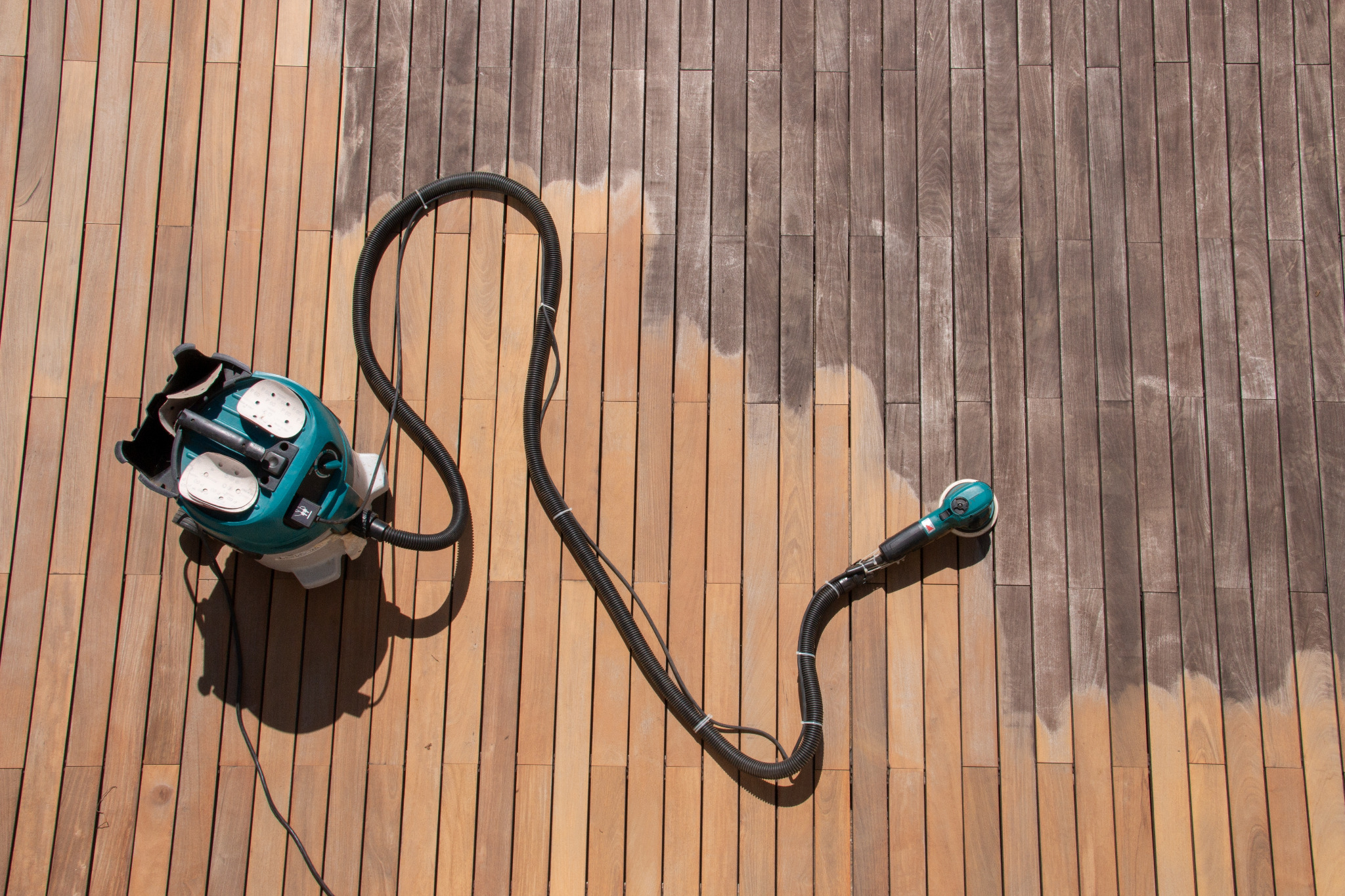 Deck sanding in Chelsea on a weathered hardwood timber decking floor, showing a clear contrast between the greyed boards and freshly sanded wood.