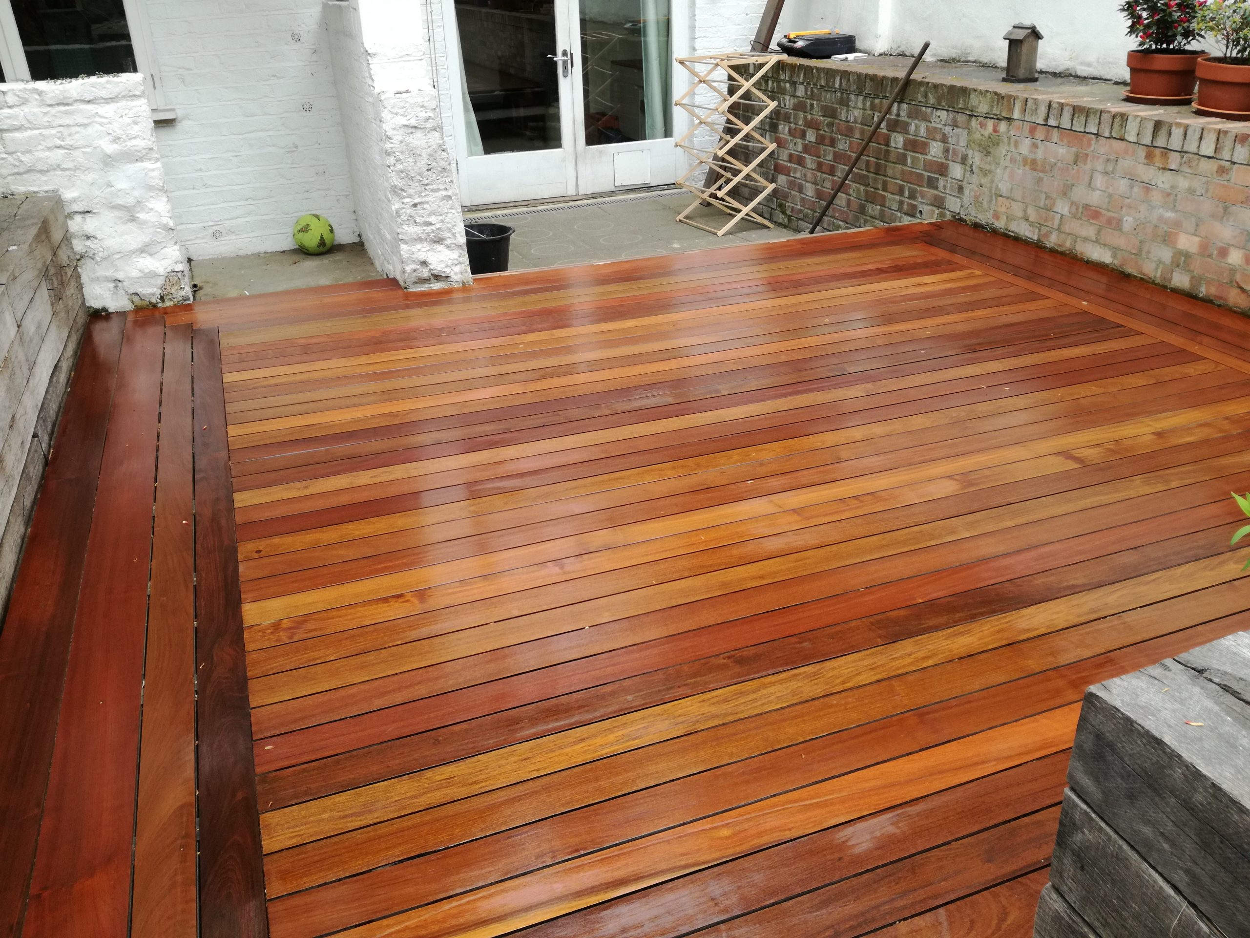Freshly restored hardwood timber garden decking floor in Chelsea after professional Deck Sanding, showing rich, smooth brown boards beside a patio.