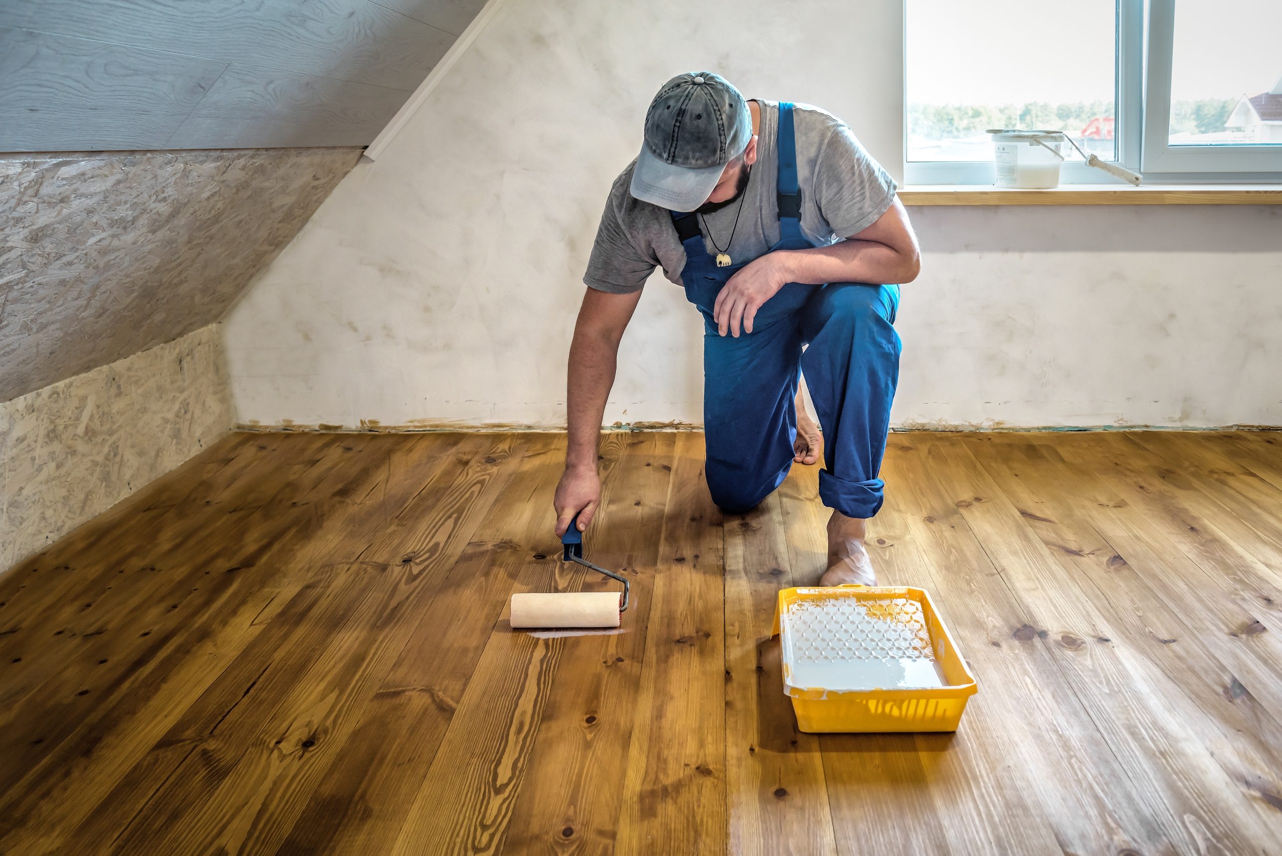 Wood Floor Sanding in Chelsea, technician applying finish to freshly sanded pine solid wood floorboards in an attic room.